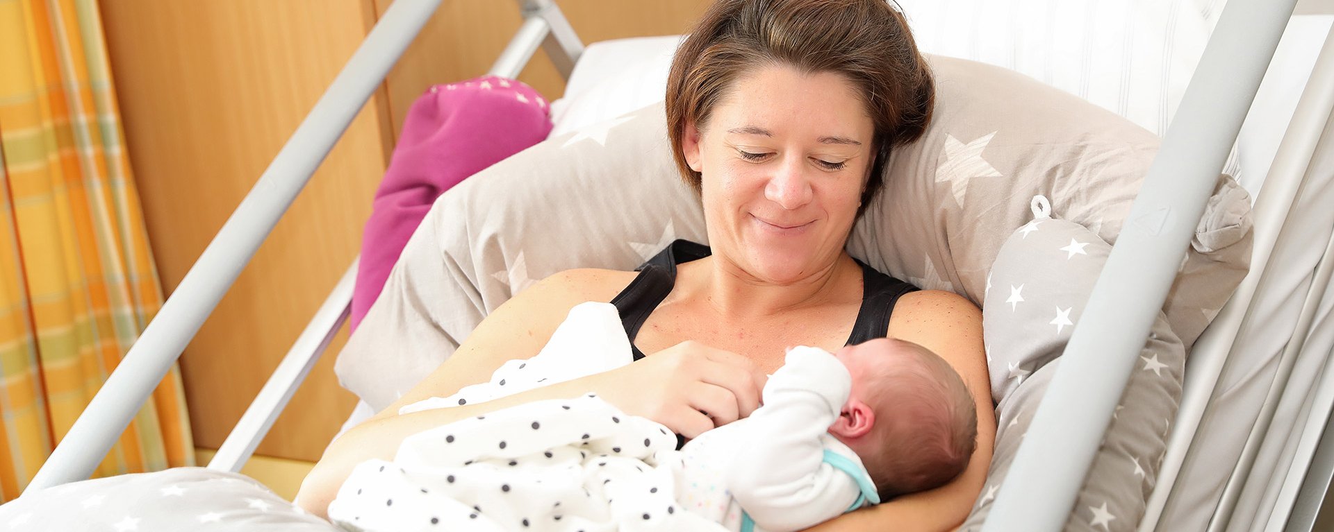 Die frisch gewordene Mutter hält ihr neugeborenes Baby im Arm. Sie liegt im Bett der Klinik Immenstadt.