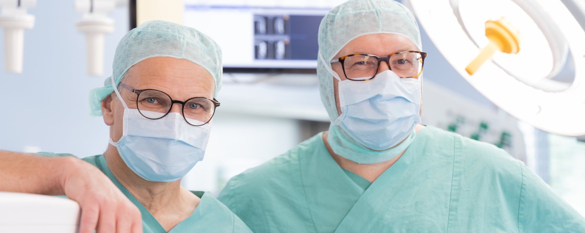 Dr. med. Roland Tines und Dr. med. Joachim Rogg, Chefärzte des Fachbereichs Gefäßchirurgie an der Klinik Immenstadt in Operationskleidung im OP-Saal