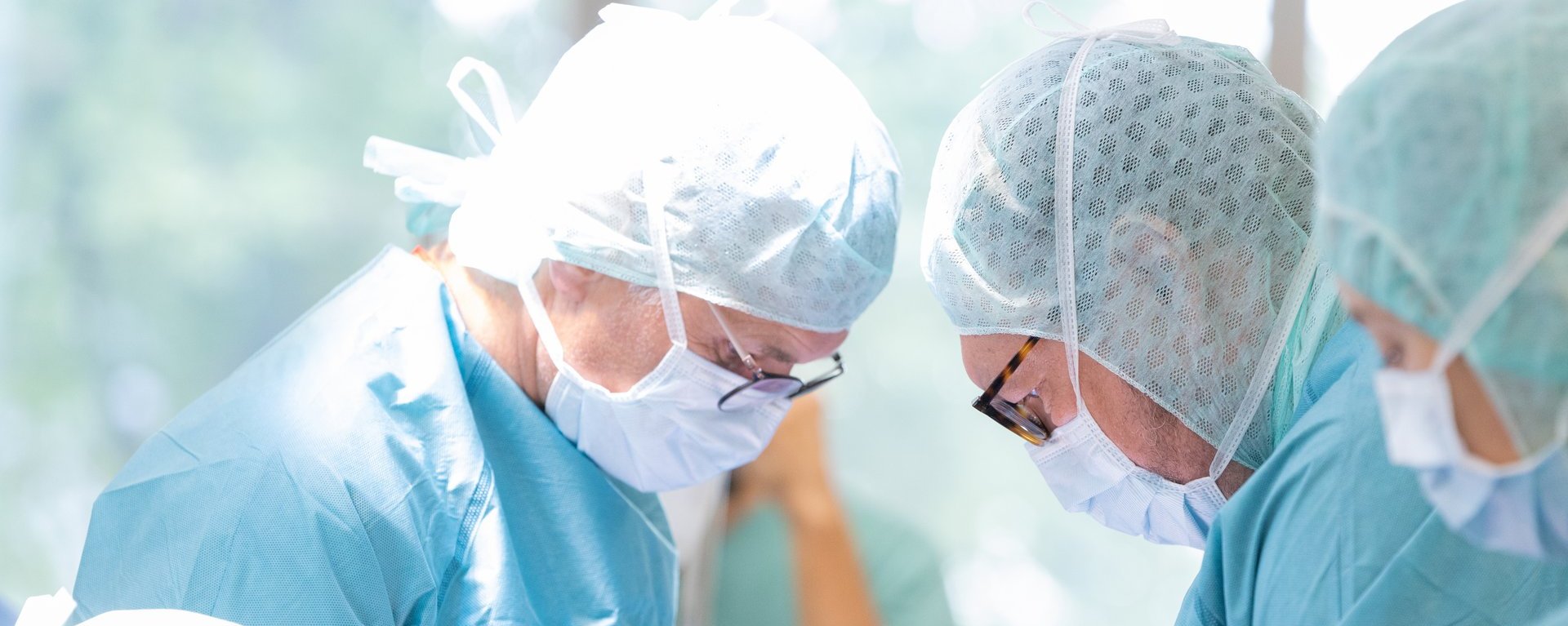 Zwei Ärzte aus dem Fachbereich Gefäßchirurgie am Klinikum Kempten beugen sich in voller Operationskleidung über einen Patienten