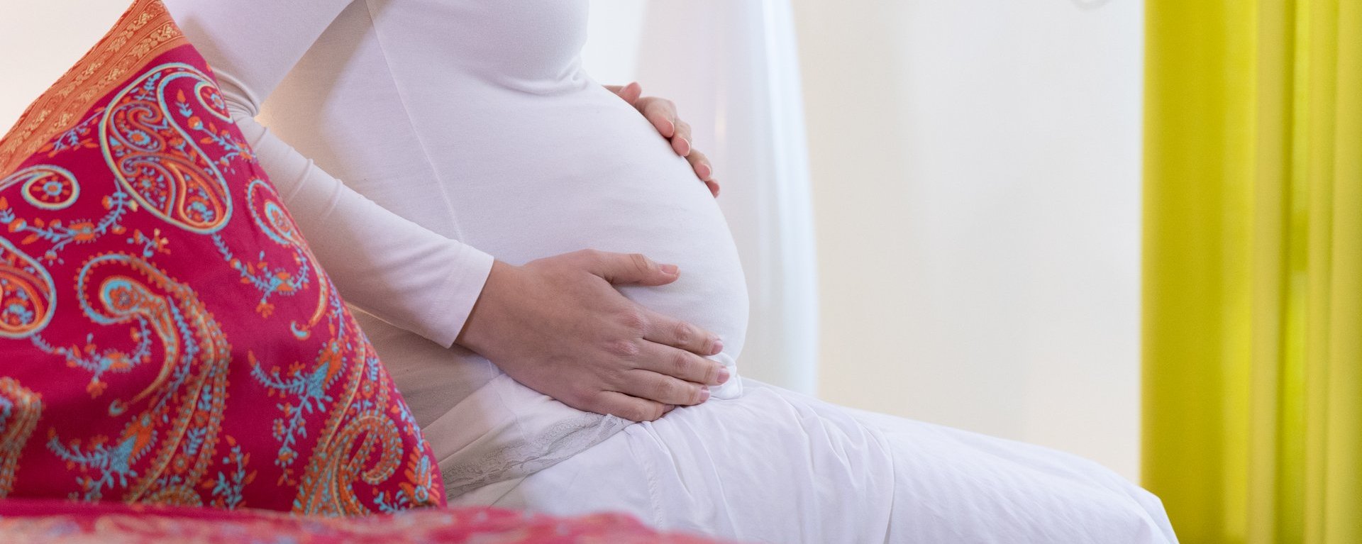 Eine sitzende, schwangere Frau berührt ihren Bauch