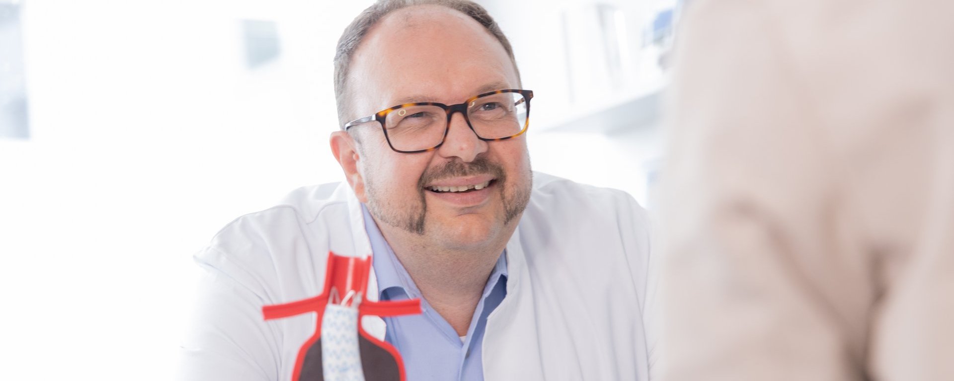 Dr. med. Roland Tines Facharzt, Chefarzt des Fachbereichs Gefäßchirurgie am Klinikum Kempten im Patientengespräch an seinem Schreibtisch