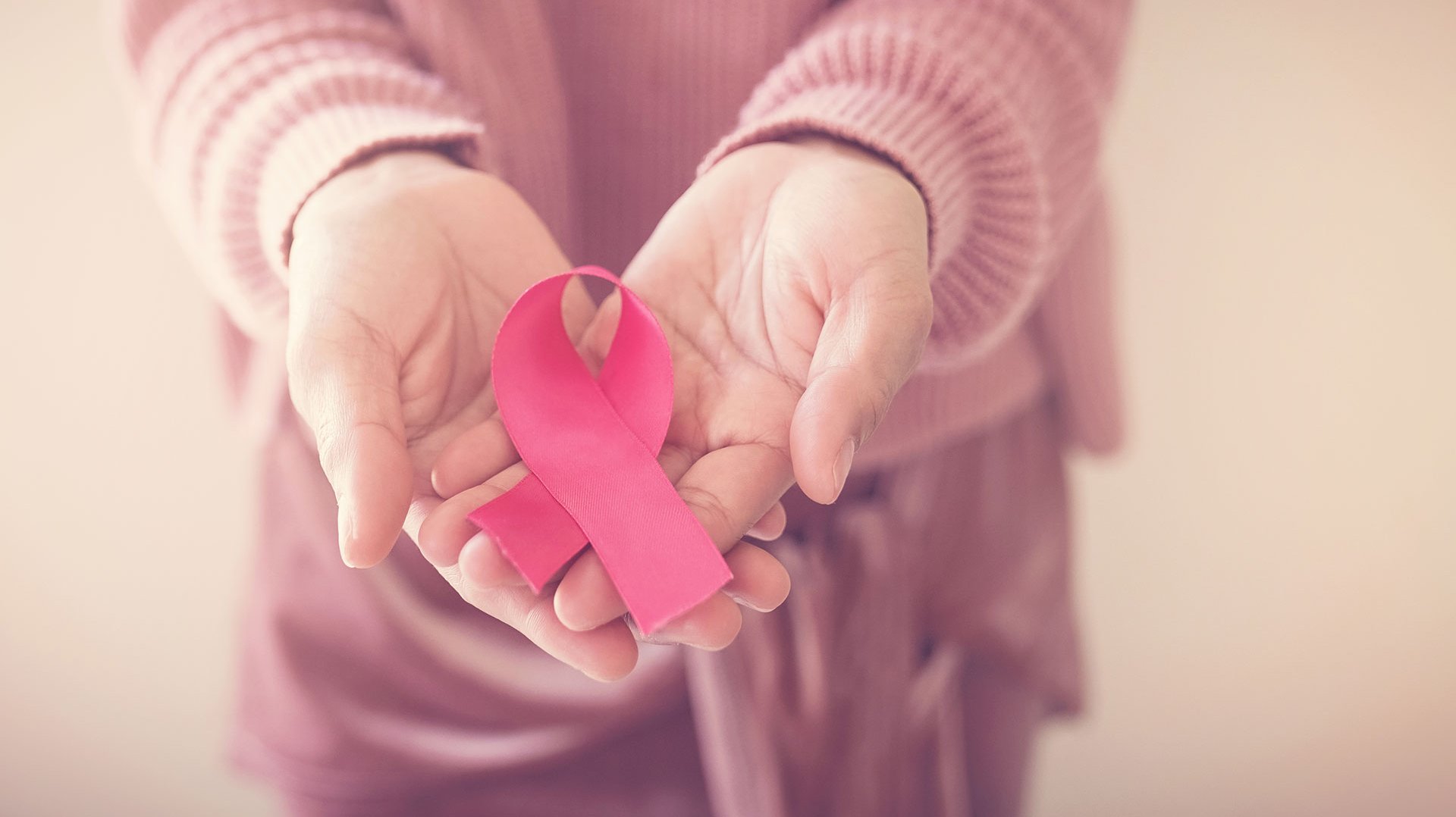 Eine Fraue hält eine rosa Schleife in Ihren Händen. Diese ist ein Symbol im Bewusstsein gegen Brustkrebs.