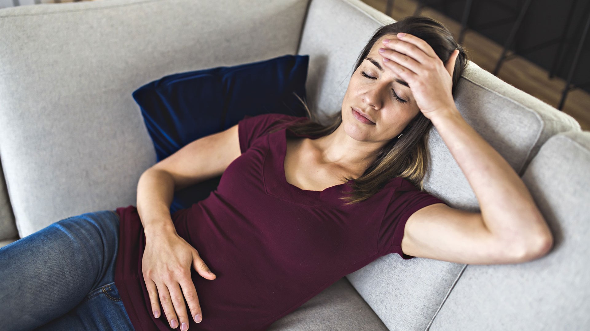 Eine Frau liegt auf der Couch und  hält sich den Bauch, da Sie wahrscheinlich Magenschmerzen hat.